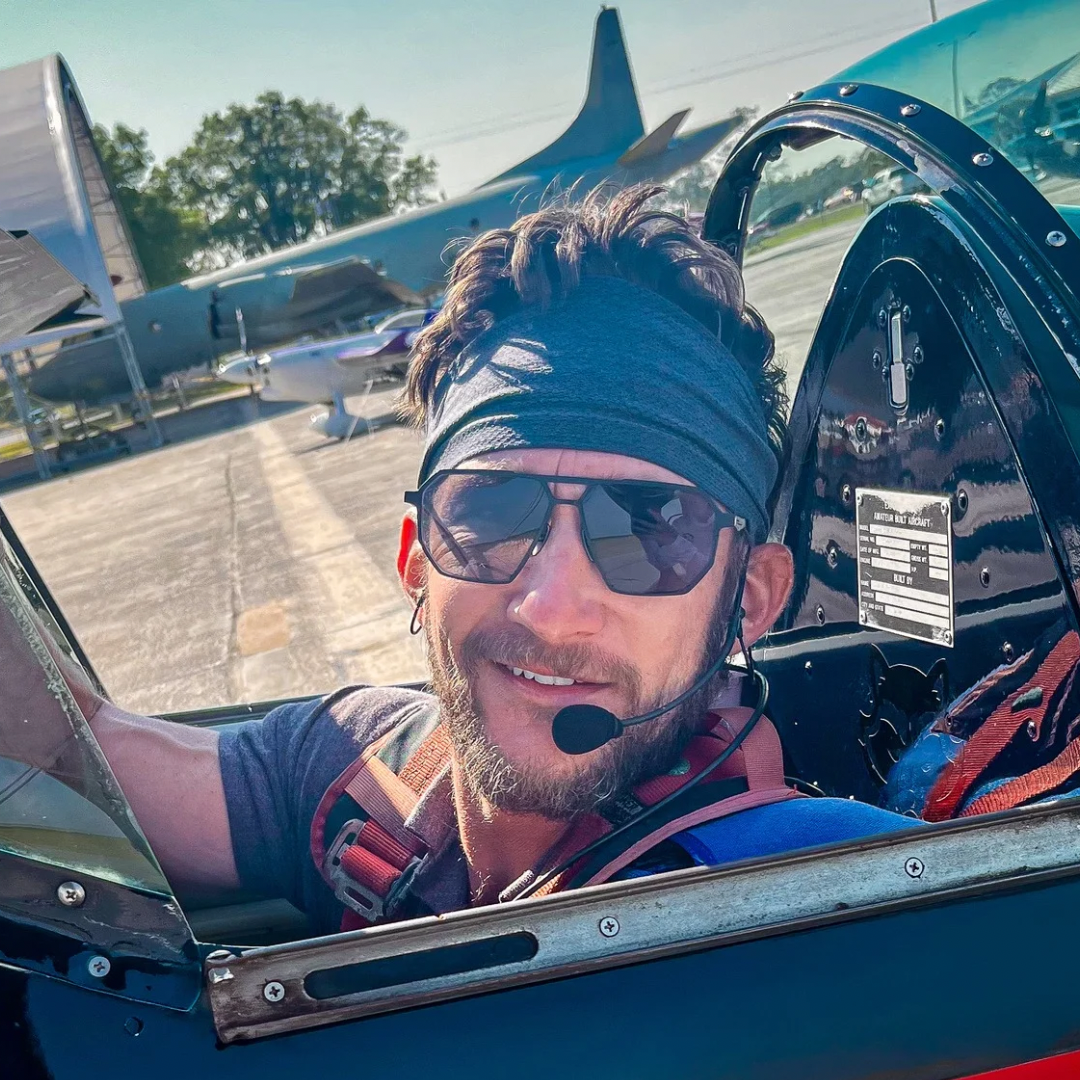 Man in Skyrift vector sunglasses and a headset inside a small airplane cockpit with another airplane in the background.